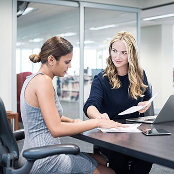 Image of two women looking at documents at an office table.